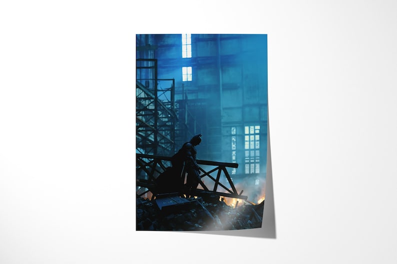 May include: A poster print featuring a silhouette of Batman standing on a wooden structure, overlooking a burning scene. The background shows a large industrial building with windows, bathed in blue and white light, creating a dramatic atmosphere.