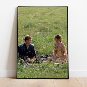 Peut inclure: Impression encadrée de deux personnes assises dans un champ herbeux. L'une porte une tenue sombre, l'autre une robe claire. La scène se déroule en extérieur, avec de l'herbe verte et un ciel clair en arrière-plan.
