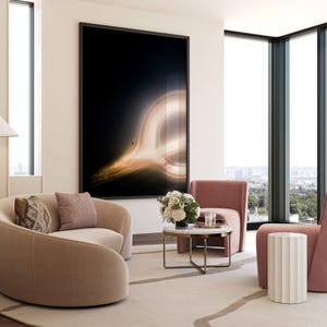 May include: A modern living room with a large framed artwork depicting a black hole. The room features two curved beige sofas with decorative pillows, two pink armchairs, a round marble coffee table, and a white side table. The room has large windows with a city view.