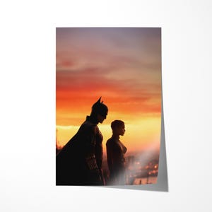 Puede incluir: Un p&oacute;ster con siluetas de dos personajes contra un atardecer vibrante. Uno est&aacute; con un disfraz de Batman, el otro con un disfraz de Catwoman. El cielo es una gradaci&oacute;n de naranja y p&uacute;rpura, con luces de la ciudad a lo lejos.