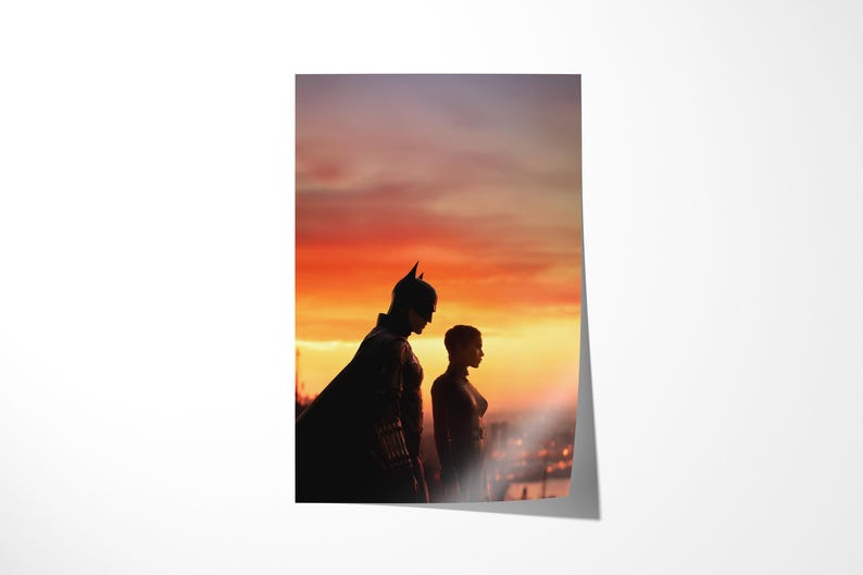 Puede incluir: Un p&oacute;ster con siluetas de dos personajes contra un atardecer vibrante. Uno est&aacute; con un disfraz de Batman, el otro con un disfraz de Catwoman. El cielo es una gradaci&oacute;n de naranja y p&uacute;rpura, con luces de la ciudad a lo lejos.
