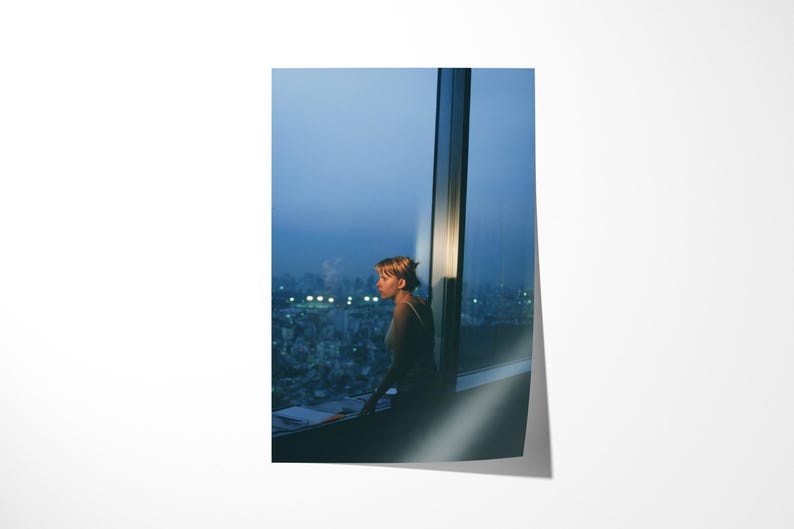 May include: A photograph of a person looking out a large window at a city skyline at dusk. The person is silhouetted against the city lights. The sky is a gradient of blues.