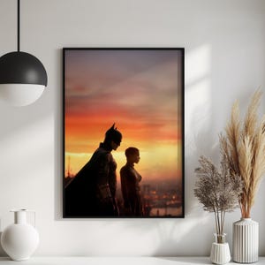 Puede incluir: Impresi&oacute;n enmarcada que presenta a Batman y Catwoman silueteados contra un atardecer vibrante. La obra de arte muestra a los ic&oacute;nicos personajes en una pose dram&aacute;tica, con un paisaje urbano visible en el fondo. La paleta de colores incluye tonos de naranja, amarillo y negro.