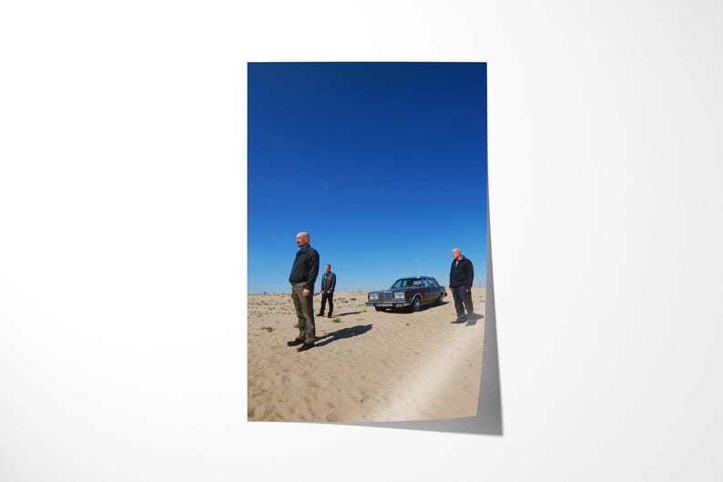 Op de afbeelding: Een posterprint met drie mannen in een woestijnlandschap, een heldere blauwe lucht en een klassieke auto. De sc&egrave;ne roept een gevoel van drama en isolement op.