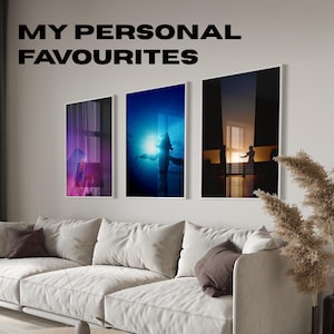 May include: Three framed art prints hanging above a white sofa. The prints feature abstract images with vibrant colors, including a figure in blue water, a silhouette at sunset, and a purple-toned image. The text "MY PERSONAL FAVOURITES" is above the prints.