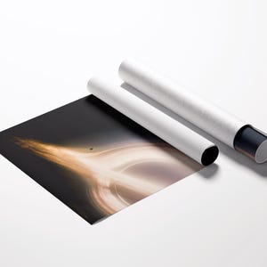 May include: A black and gold art print depicting a black hole, partially rolled, with two white cylindrical tubes. The tubes have black and gray end caps. The print is on a white surface.