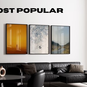 Puede incluir: Tres impresiones art&iacute;sticas enmarcadas cuelgan sobre un sof&aacute; seccional de cuero negro. Las impresiones presentan escenas abstractas y de paisajes. El texto "MOST POPULAR" se muestra encima de la obra de arte. Una mesa negra, sillas y una l&aacute;mpara de pie completan el moderno sal&oacute;n.