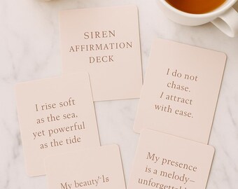 Könnte beinhalten: Ein Siren Affirmation Deck mit inspirierenden Zitaten, eine brennende Kerze in einem Glas und eine Tasse Tee auf einer Marmoroberfläche. Das Deck enthält Karten mit Sätzen wie "Ich erhebe mich sanft wie das Meer, doch kraftvoll wie die Gezeiten."