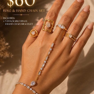 May include: A gold-toned ring and hand chain set. The set includes five stackable rings and a hand chain bracelet. The rings feature various gemstone designs. The hand chain connects to a bracelet with a teardrop-shaped gem.