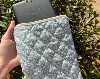 Könnte beinhalten: Eine gesteppte Kindle-Hülle aus hellgrünem Stoff mit weißem Blumenmuster. Die Hülle hat ein Rautenmuster und einen cremefarbenen Reißverschluss. Ein Amazon Kindle befindet sich in der Hülle.