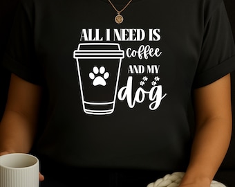 May include: Black t-shirt with the text "ALL I NEED IS coffee AND MY dog" in white. A white graphic of a coffee cup with a paw print is also featured. The shirt is a casual style.