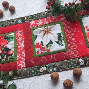 Op de afbeelding: Een feestelijke kersttafelloper met poinsettia's en hulst. De loper heeft een rood-groen kleurenschema met bloemen- en sneeuwvlokpatronen. De loper is ongeveer 30 cm breed en 122 cm lang.