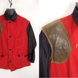 May include: A red, black, and brown shooting jacket with a leather shoulder patch and a yellow embroidered letter 'A' on the front.