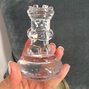 Könnte beinhalten: Transparente Glas-Rochade-Schachfigur mit detailliertem Gesicht und burgähnlicher Spitze. Der Sockel ist rund und mit "KOSTA BODA SINCE 1742" gekennzeichnet. Das Glas ist transparent.
