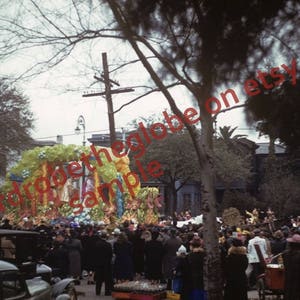 Könnte beinhalten: Ein Vintage-Foto von einer Mardi Gras-Parade in New Orleans, Louisiana. Die Parade zeigt einen großen, farbenfrohen Wagen mit kostümierten Menschen. Der Wagen ist mit Blumen, Perlen und anderen festlichen Dekorationen geschmückt. Die Menge jubelt und winkt, als der Wagen vorbeifährt.