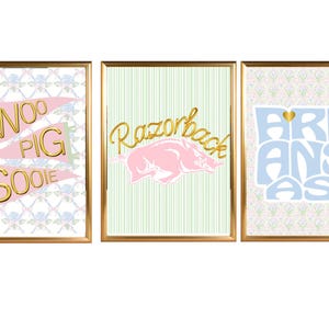 May include: Three framed prints with gold frames. The prints feature the words "Woo Pig Sooie", a pink Razorback, and the state of Arkansas in blue. The backgrounds have floral and striped patterns.