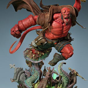 Op de afbeelding: Een dynamisch beeld van Hellboy, een rood geschilderde demonachtige figuur, die een vlammend zwaard hanteert. Hij poseert in een sprong boven een gedetailleerde basis met groteske, buitenaardse elementen. De figuur draagt een bruine jas en korte broek.
