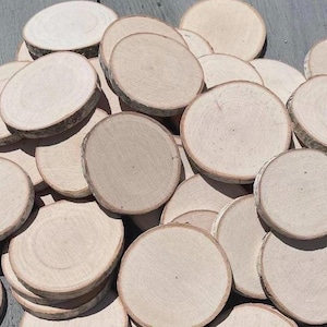 May include: A large collection of circular, light-colored wooden discs with natural bark edges. Each piece features a smooth, sanded surface showing the light grain of the wood, arranged in an overlapping pile to display their varied sizes.