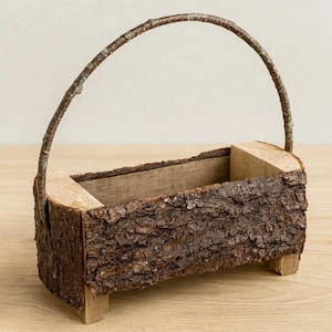May include: A rustic wooden basket with a bark-covered exterior and a curved branch handle. The rectangular container sits on small wooden feet. The natural brown tones and textured surface create a charming, handcrafted aesthetic.