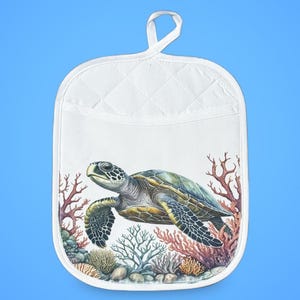 May include: White quilted oven mitt featuring a detailed illustration of a sea turtle swimming near coral. The turtle has a green and brown shell, with a light blue background. The mitt has a loop for hanging.