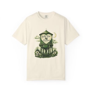 May include: Cream-colored t-shirt featuring a green and white illustration of a water tower with the words "Billy Bob loves Charlene" inside a heart. The design includes clouds, a moon, and flowers.