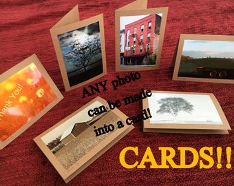 May include: A collection of six cards with different images printed on them. The cards are made of brown paper and have a white border. The images include a field of yellow flowers, a tree in a field, a building with a red facade, a field with a barn, a tree in a field, and a field with a tractor. The text "ANY photo can be made into a card! CARDS!!" is written on the cards.
