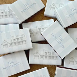 May include: A collection of light blue and white striped boxes with a house illustration and the text "The Seymours" in a soft blue font. The boxes are arranged on a wooden surface.
