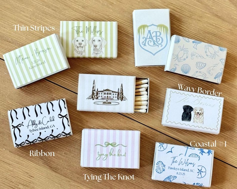 May include: A collection of decorative matchboxes with various designs. Some boxes feature text like "Thin Stripes," "The Millers," and "Abby & Caleb." Other designs include illustrations of dogs, coastal themes, and a ribbon motif. The matchboxes are on a wooden surface.
