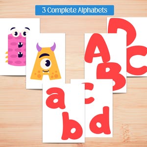 May include: Educational flashcards featuring the alphabet. The cards display uppercase and lowercase letters in red, along with whimsical monster illustrations for each letter. The text "3 Complete Alphabets" is at the top.