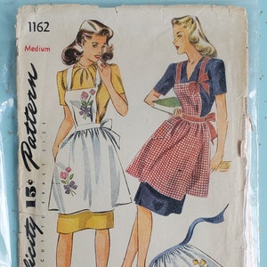 May include: Vintage Simplicity sewing pattern 1162 for a medium-sized apron. The pattern shows two women wearing different styles of aprons, one with a floral print and the other with a gingham pattern. The pattern includes instructions for making a gathered apron with a tie.