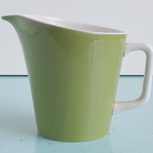 Puede incluir: Una jarra de cer&aacute;mica verde con asa blanca y interior blanco. La jarra tiene una forma redondeada ligeramente acampanada.