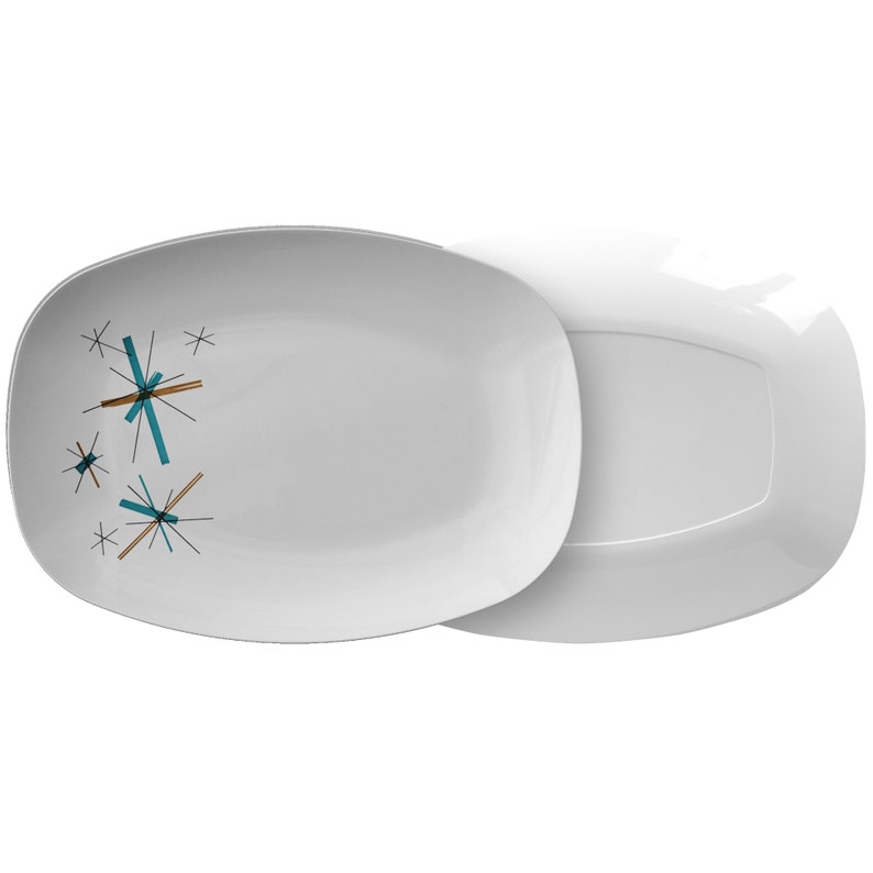 May include: A white oval serving platter with a teal and brown starburst design. The platter is shown with a matching white oval platter underneath.