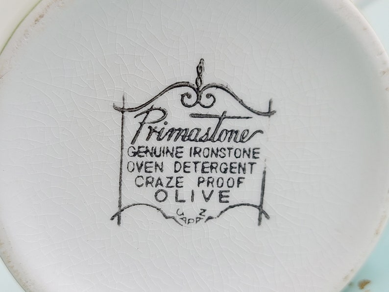 Puede incluir: Primer plano de la parte inferior de un plato de cer&aacute;mica blanco con un logotipo en blanco y negro que dice "Primastome Genuine Ironstone Oven Detergent Craze Proof Olive".