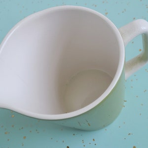 Puede incluir: Una jarra de cer&aacute;mica verde con interior blanco y asa. La jarra est&aacute; vac&iacute;a y tiene un ligero labio en el lado del vertido.