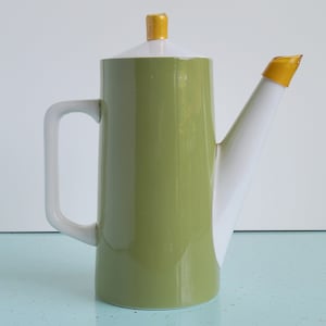 May include: A green and white ceramic coffee pot with a yellow lid and spout. The pot has a modern design and is perfect for serving coffee or tea.