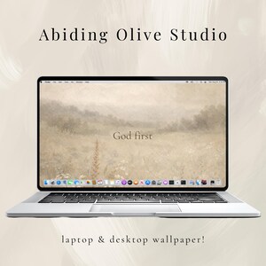May include: A silver laptop displays a serene landscape wallpaper with the words "God first." The screen is surrounded by a black bezel. The text "Abiding Olive Studio" and "laptop & desktop wallpaper!" are also visible.