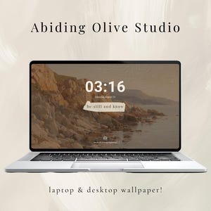 May include: A silver laptop displaying a scenic desktop wallpaper with a coastal landscape. The time 03:16 is visible, along with the text "be still and know." The words "Abiding Olive Studio" and "laptop & desktop wallpaper!" are also displayed.
