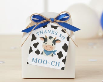 May include: A white gift box with a blue ribbon and a tag that says "THANKS SO MOO-CH." The tag features a cartoon cow with a blue bandana and black spots. The box is tied with twine.
