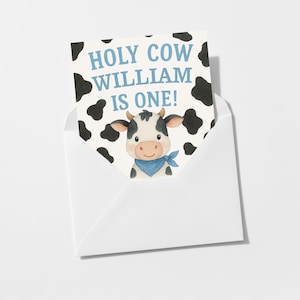 May include: A white envelope holding a birthday card. The card shows a cartoon cow wearing a blue bandana, with the text "HOLY COW WILLIAM IS ONE!" in blue. The card has a white background with black cow spots.