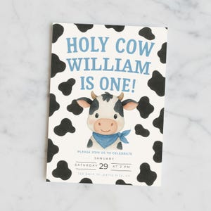 May include: A rectangular invitation card with a light blue background and black cow spots. The text "HOLY COW WILLIAM IS ONE!" is in blue. A cartoon cow with a blue bandana is in the center. The card also includes party details.
