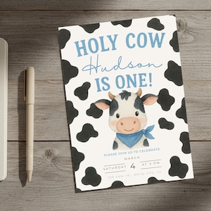 May include: A white invitation card featuring a cow design. The text "HOLY COW Hudson IS ONE!" is in blue, with a cartoon cow illustration. Black cow spots surround the text. The invitation includes event details.