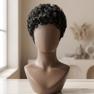 Könnte beinhalten: Eine kurze, schwarze Perücke mit engen, definierten Locken in einem Pixie-Schnitt. Die Perücke wird auf einem glatten, gesichtslosen, hellbraunen Schaufensterpuppenkopf mit Hals und Schultern präsentiert, der die Haarstruktur und das Volumen zeigt.