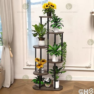 Könnte beinhalten: Ein mehrstöckiger Pflanzenständer mit dunkelbraunen Regalen und schwarzen Metallstützen. Der Ständer beherbergt verschiedene Topfpflanzen, darunter Sonnenblumen und Farne. Der Text "GREENHAVENSTANDS" ist sichtbar.