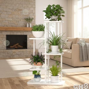 Op de afbeelding: Een witte, meerlaagse plantenstandaard met diverse potplanten. De standaard heeft een rechthoekige vorm met meerdere planken. De planten omvatten bladgroene planten en bloeiende planten. De standaard staat in een woonkamer.