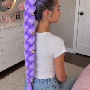 May include: A long, braided lavender wig with gold flower embellishments. The wig is styled in a high ponytail. The person is wearing a white t-shirt and blue jeans. The wig is from Veloura Wigs.