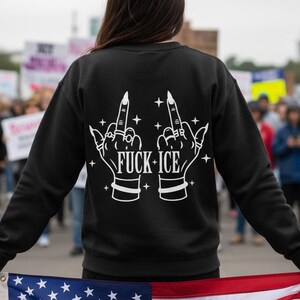 May include: Black sweatshirt with a white graphic on the back. The graphic shows two hands with middle fingers raised, stars, and the text "FUCK ICE".