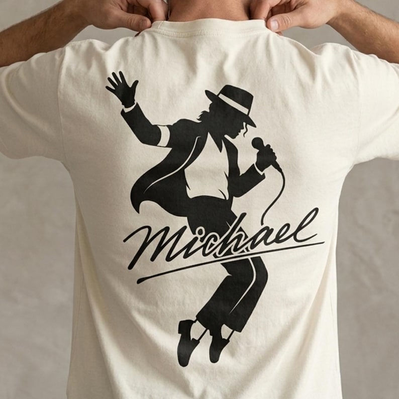 Puede incluir: Camiseta color crema con una silueta negra de un cantante con fedora y micr&oacute;fono. La palabra "Michael" est&aacute; escrita en cursiva debajo. El dise&ntilde;o est&aacute; centrado en la parte posterior.
