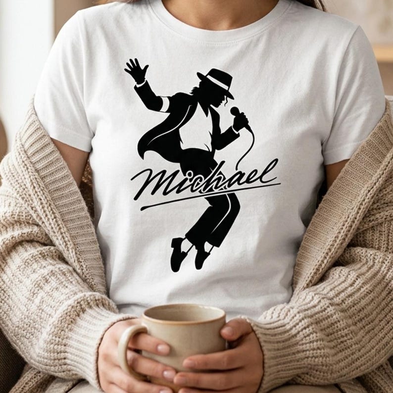 Puede incluir: Camiseta blanca con una silueta negra de un artista con sombrero y traje, sosteniendo un micr&oacute;fono. El nombre "Michael" est&aacute; escrito en cursiva debajo. La camiseta es de cuello redondo cl&aacute;sico.