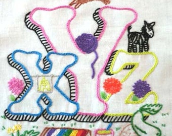 Puede incluir: Letras bordadas del alfabeto X, Y y Z en rosa, azul, verde y amarillo con contornos negros. Las letras están decoradas con flores, una cabra, un gato y una bola de lana. También hay un pincel, una taza de pintura y una bandeja de lápices de colores.
