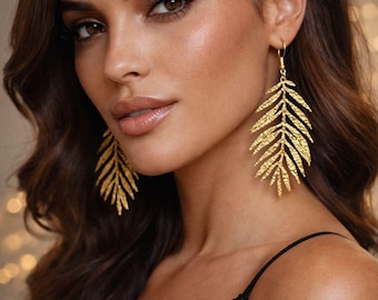 May include: Gold-colored leaf-shaped earrings. The earrings are dangling and have a textured surface. The model is wearing a black sequined top. The background is blurred with bokeh lights.